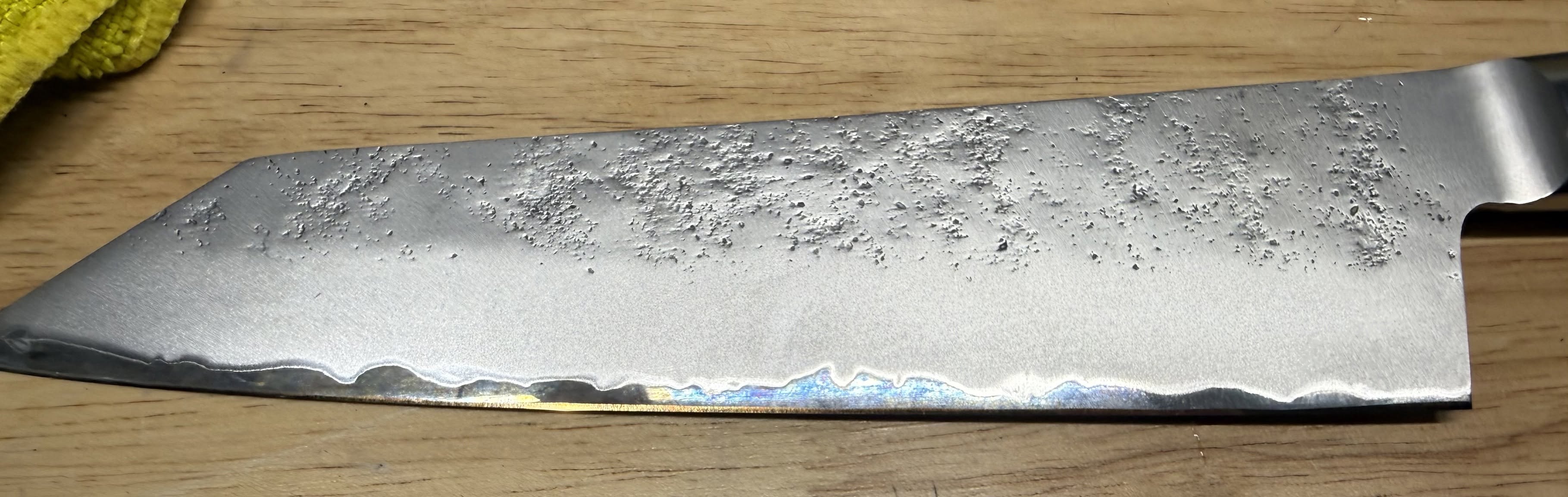 Close-up of a textured kitchen knife blade and polished cutting edge on a wooden surface